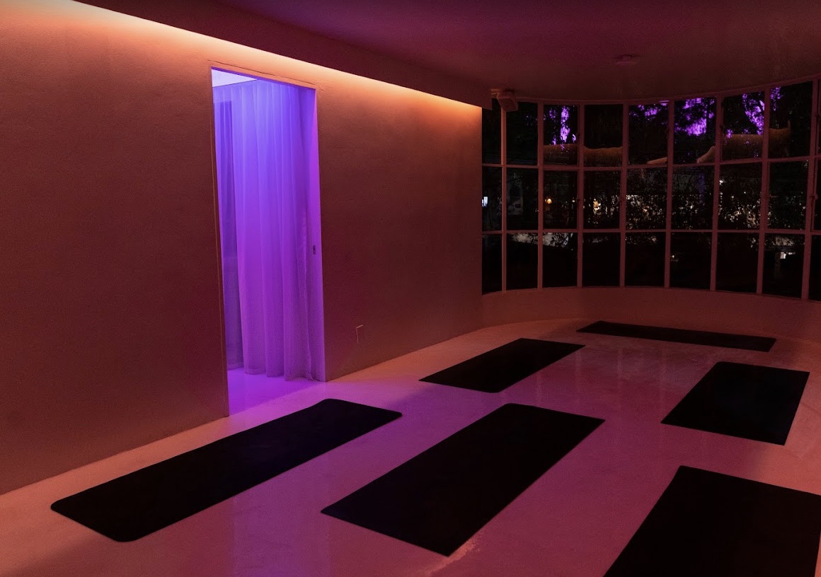 Salón de One Percent Yoga con tapetes e iluminación cálida y violeta